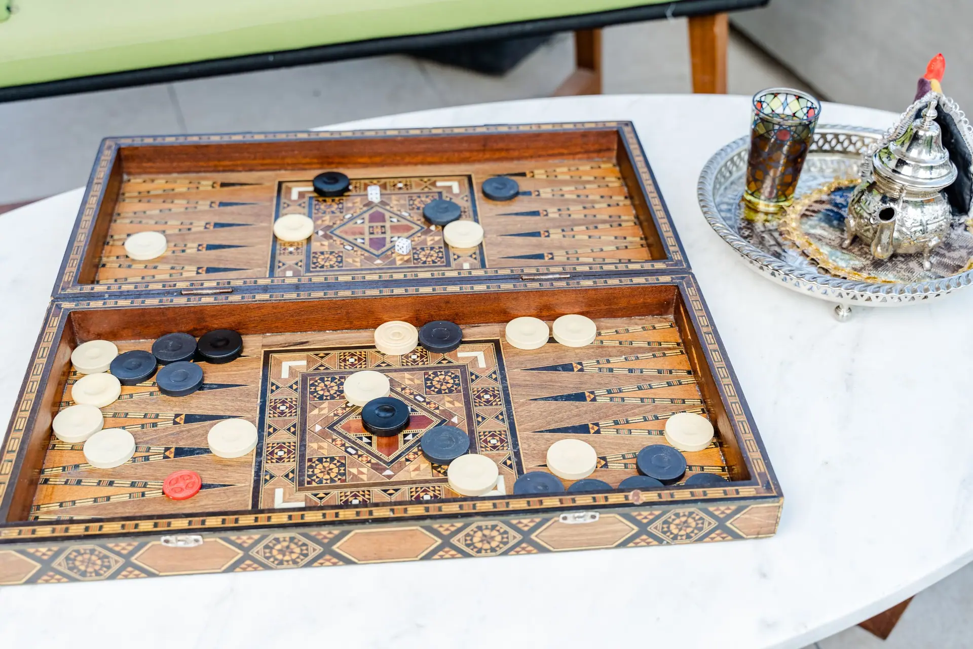 Intricate backgammon board and Moroccan tea set on a marble table, showcasing Middle Eastern culture.